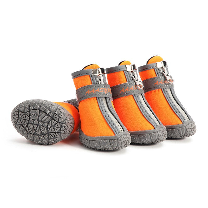 Dog wearing orange waterproof rain boots on muddy trail